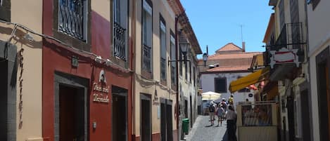 A cobblestone street lined with buildings, some with balconies and awnings, under a clear blue sky.