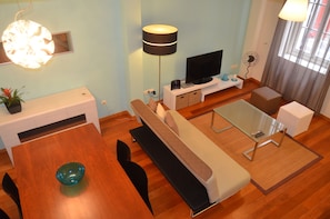 Uma sala de estar moderna com sofá, mesa de centro de vidro, mesa de jantar com cadeiras, televisão e luminária.
