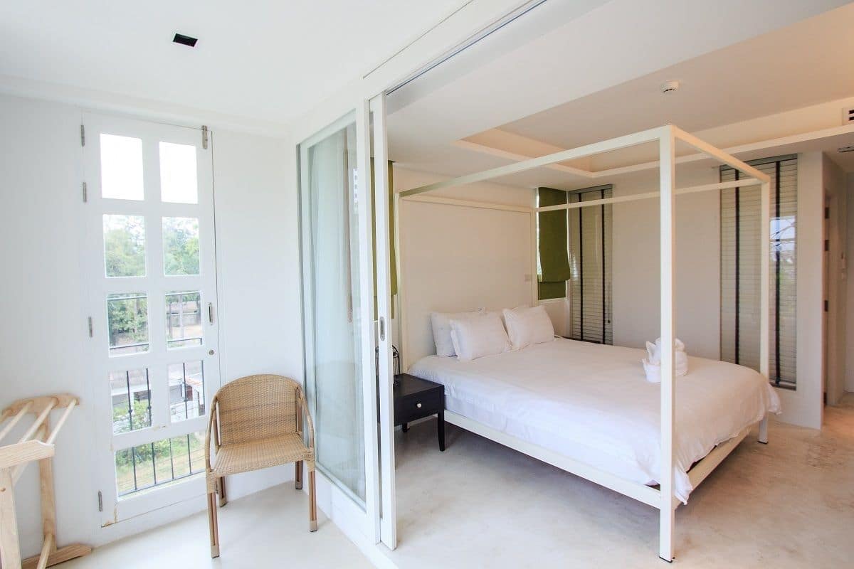 Un dormitorio con cama con dosel, una silla, una mesita de noche y un ventanal corredero que da a un espacio exterior.