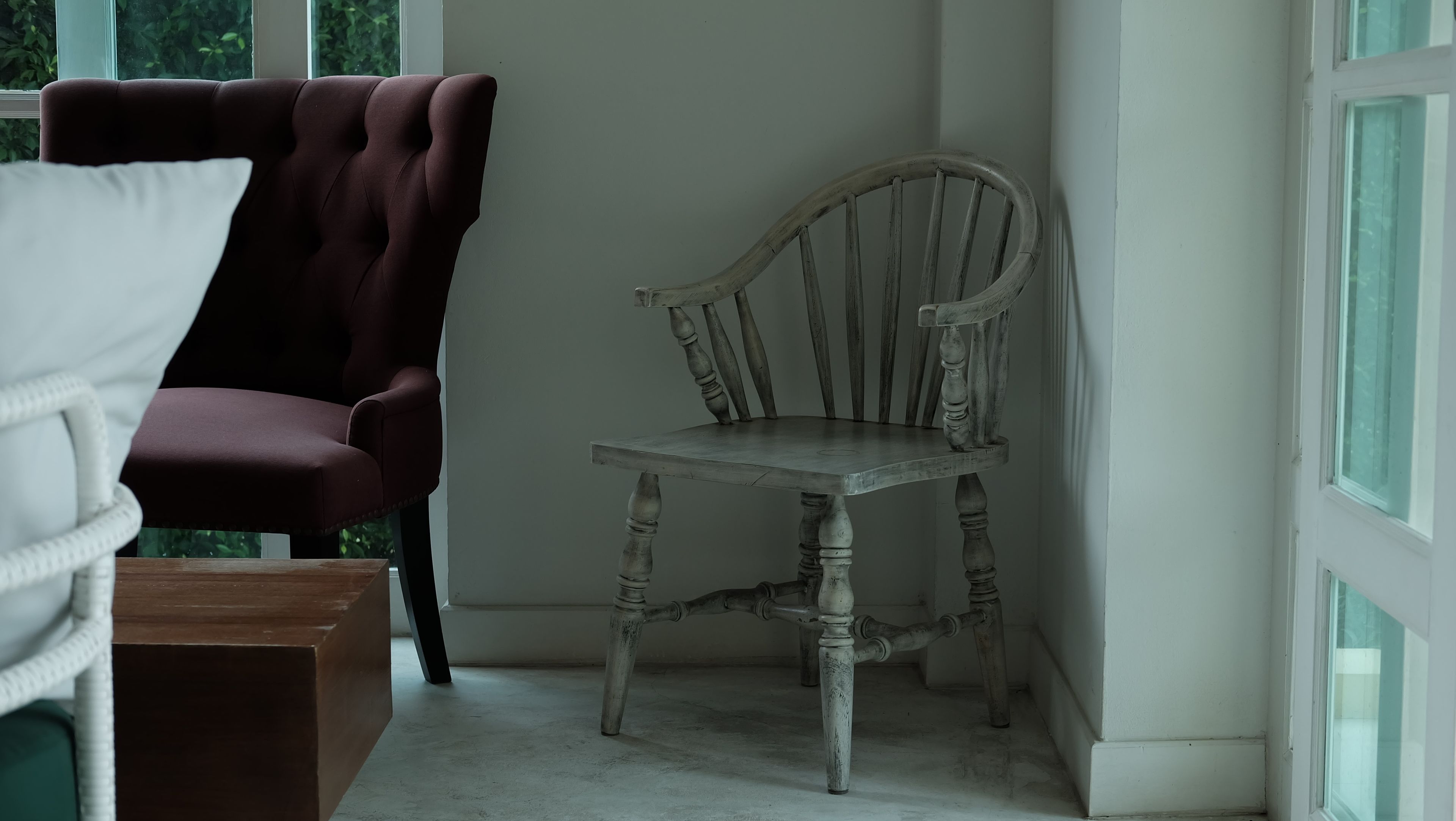 Una habitación con una silla de madera, un sillón mullido y una mesa de madera.