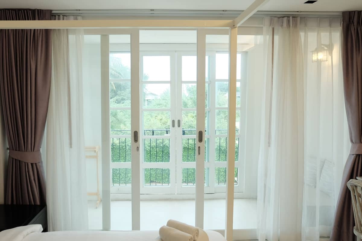 Habitación de hotel con cama, una mesita y vistas a un balcón con vegetación.