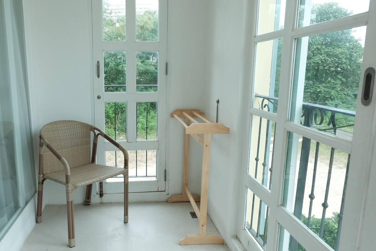 Una habitación con una silla de mimbre, un atril de madera y grandes ventanales con vistas a la vegetación.