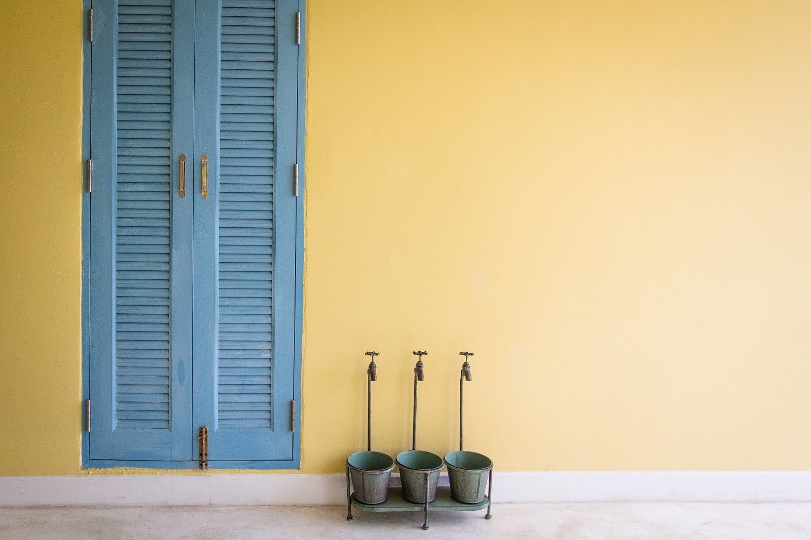 A room with a blue door, a yellow wall, and three metal buckets on a small table.