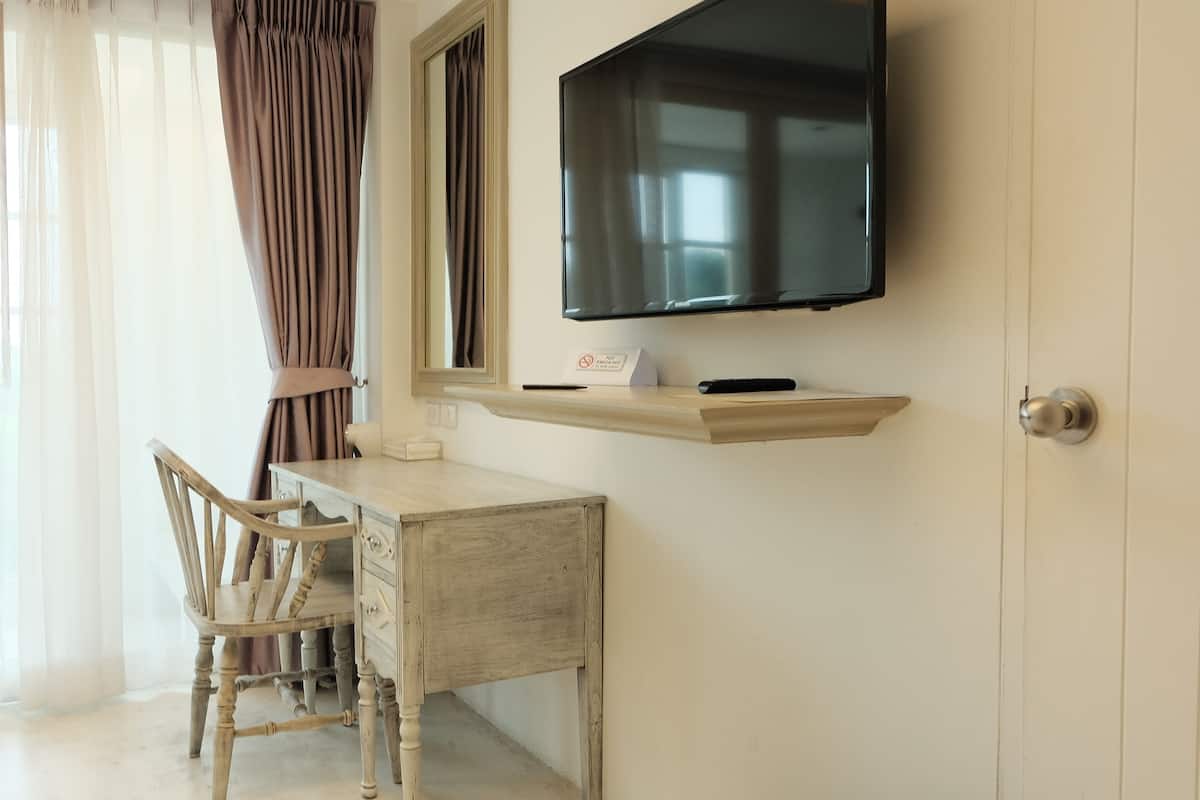 Una habitación con escritorio de madera, una silla, televisor montado y ventana con cortinas.