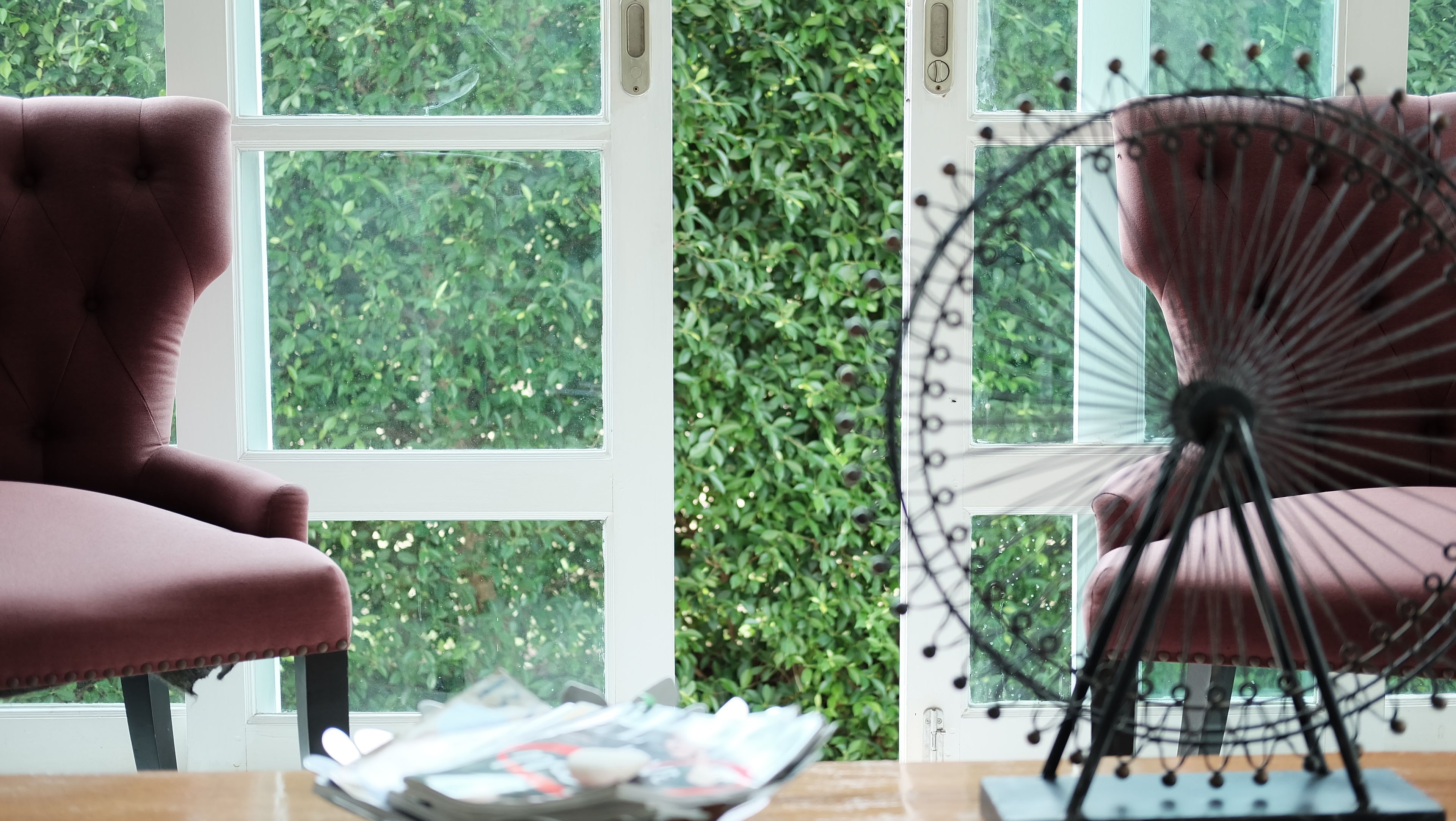 A room with a pink chair, a table with magazines, and a window with a view of greenery.