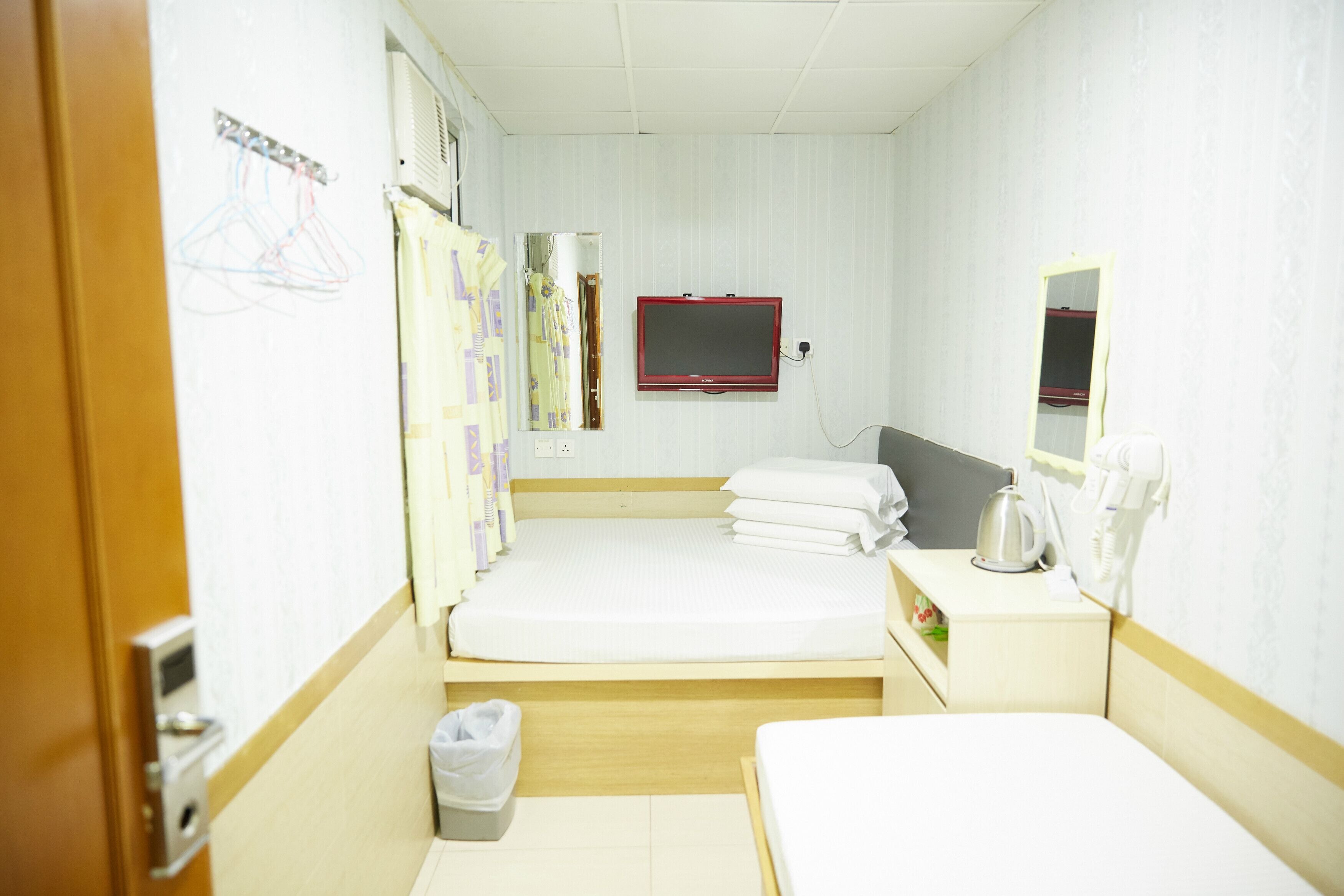 Habitación de hotel con dos camas, una mesita de noche con hervidor, un espejo y televisor montado en la pared.