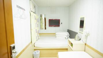 Habitación de hotel con dos camas, una mesita de noche con hervidor, un espejo y televisor montado en la pared.