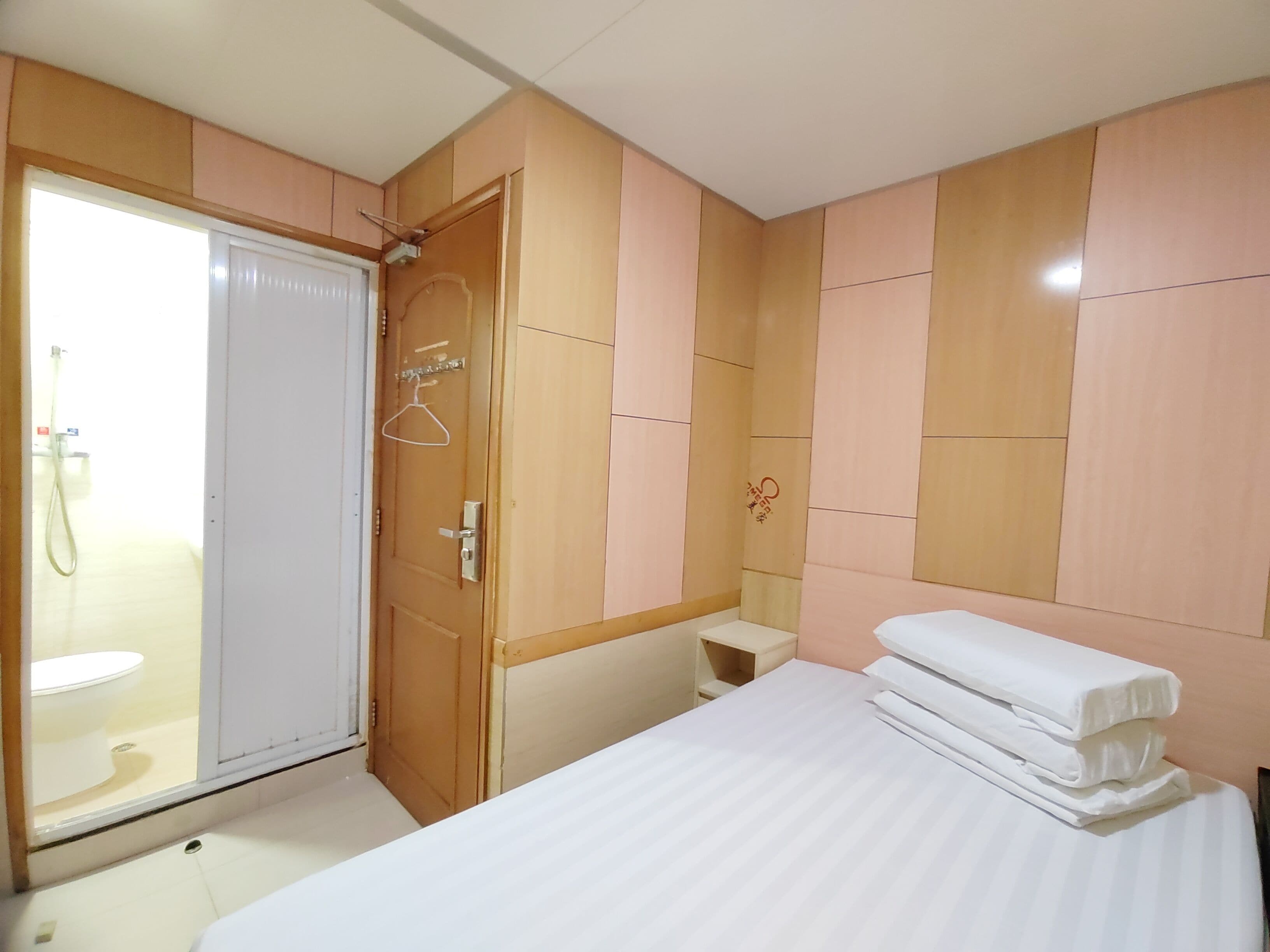 A hotel room with a bed, a bedside table, a wardrobe, and a shower area.