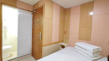 A hotel room with a bed, a bedside table, a wardrobe, and a shower area.