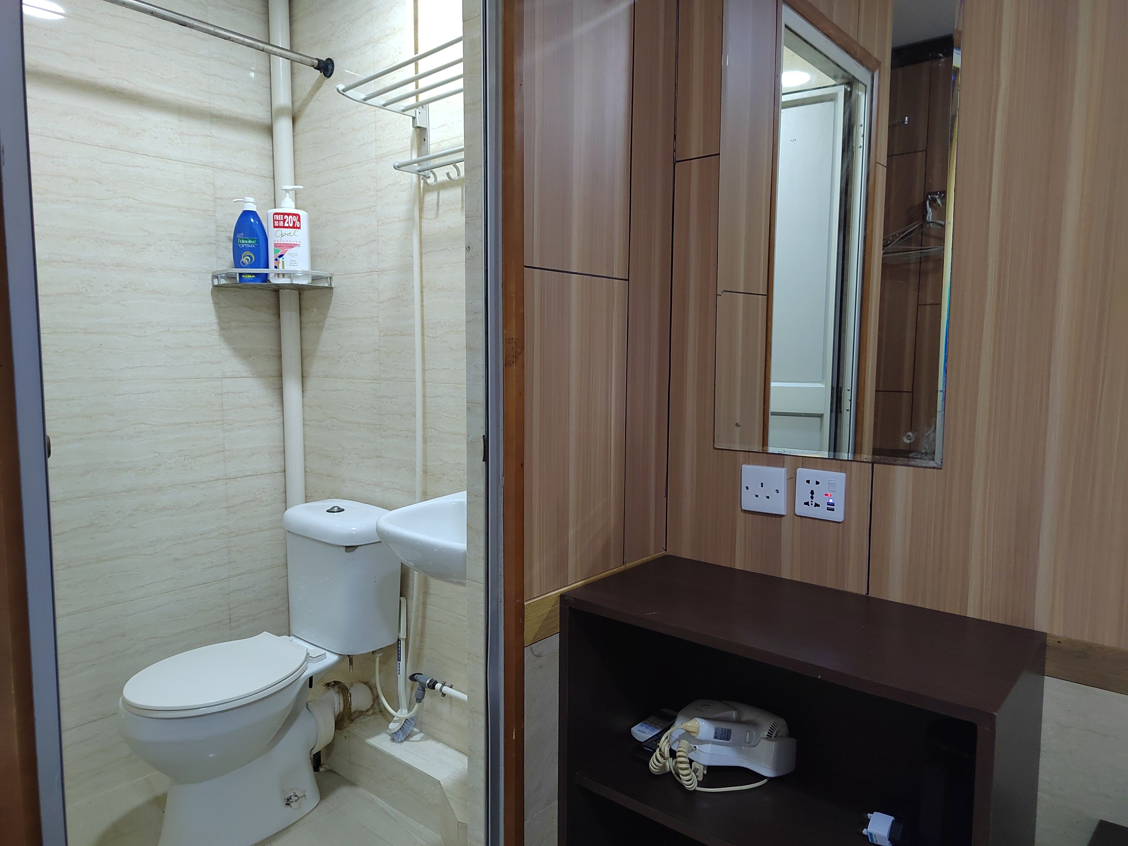 A bathroom with a toilet, a hand dryer, a shelf with toiletries, and a mirror.