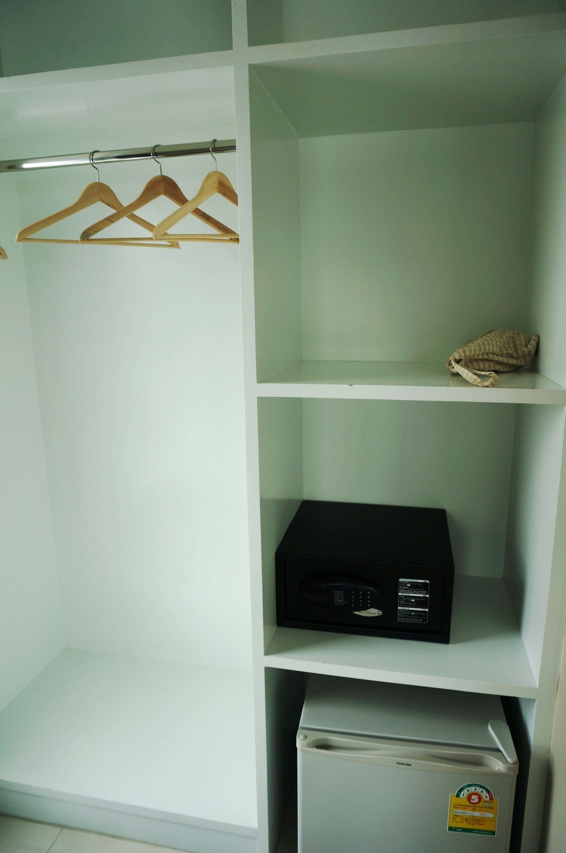 A closet with three wooden hangers, a microwave, and a refrigerator.