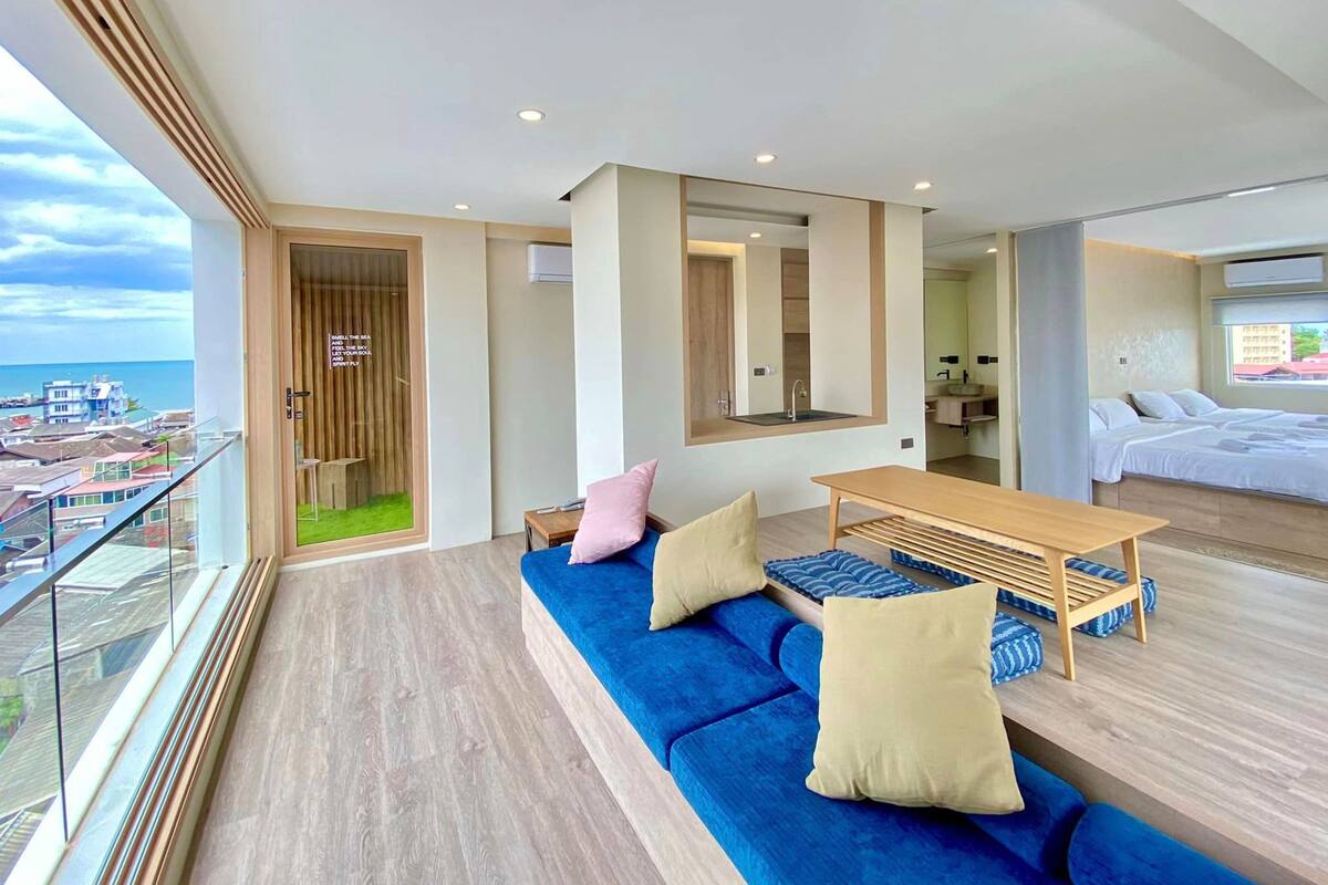 A modern hotel room with a balcony, a large bed, a wooden table, and a blue sofa.