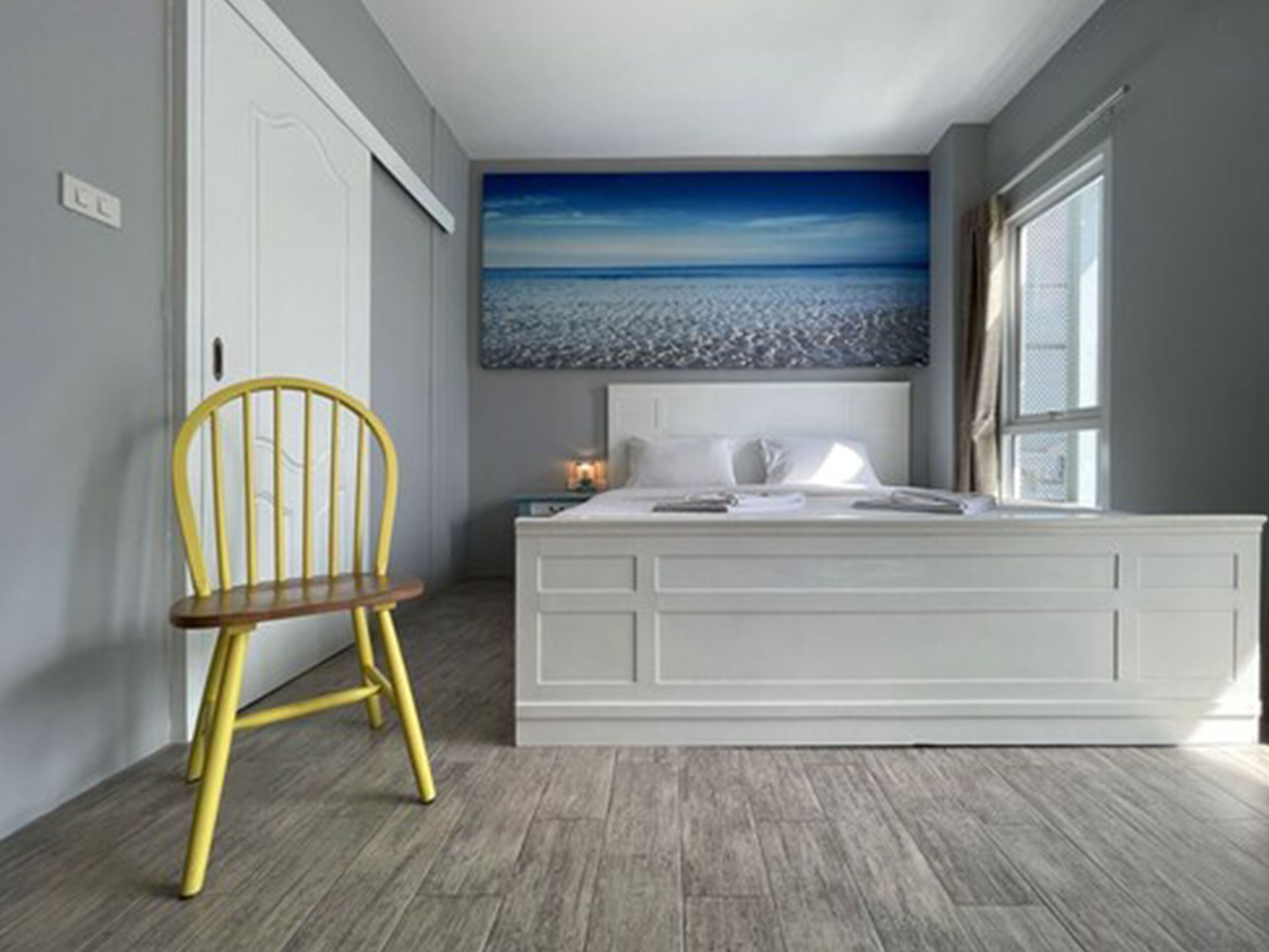 A bedroom with a bed, a chair, a nightstand, and a large painting of a beach scene.