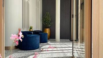 A modern hallway with a glass door, a potted plant, and blue seating.