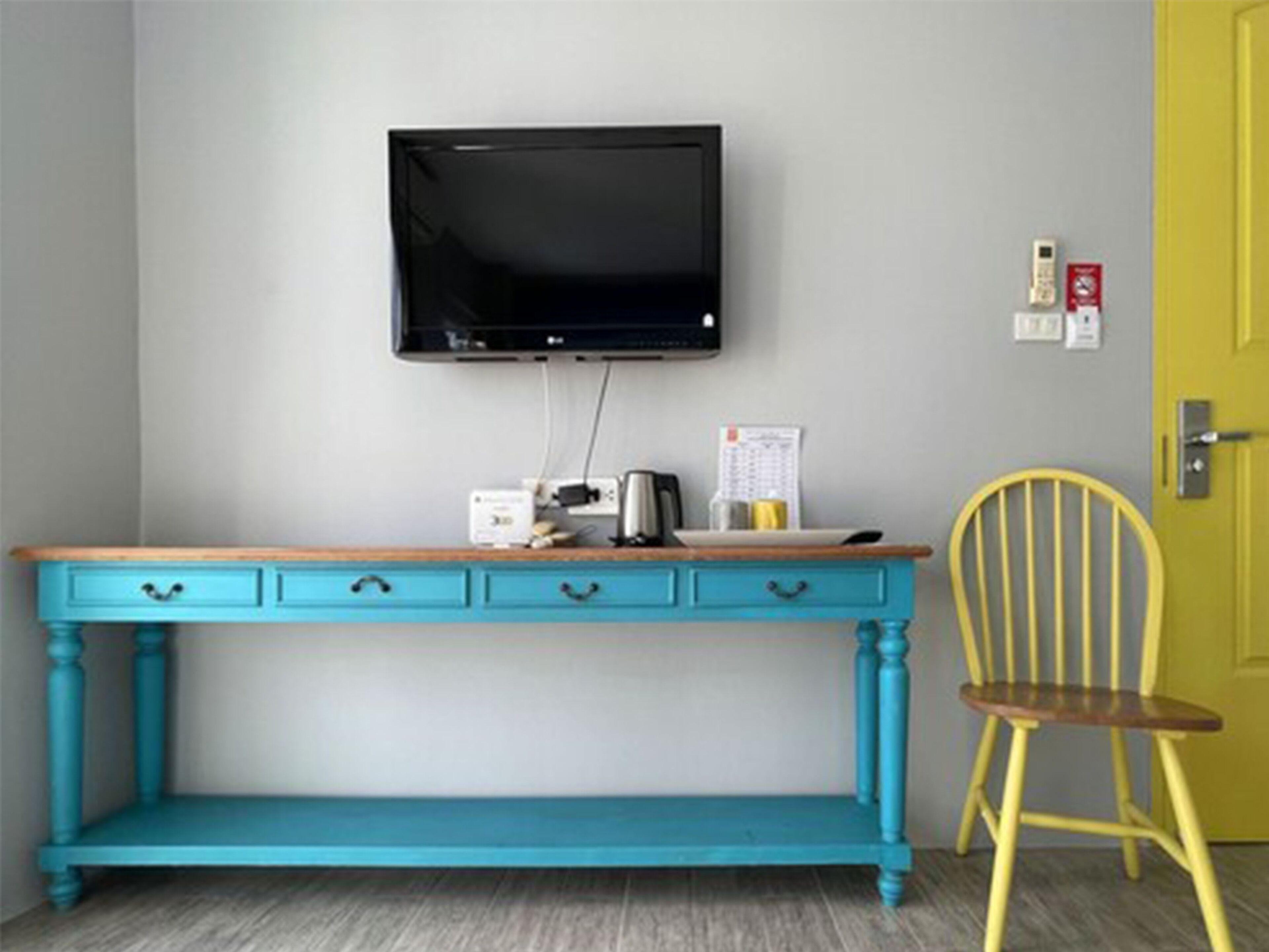 A teal desk with drawers, a mounted television, and a yellow chair.