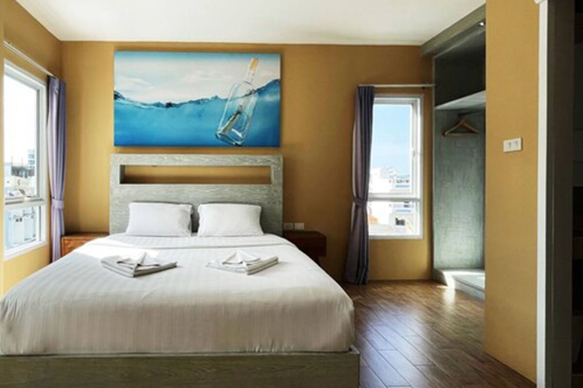 A hotel room with a bed, a painting of a bottle in water, a window, and a bathroom door.