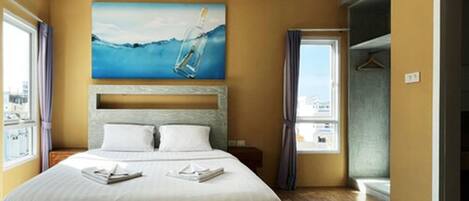 Une chambre d’hôtel avec un lit, un tableau représentant une bouteille dans l’eau, une fenêtre et une porte de salle de bain.