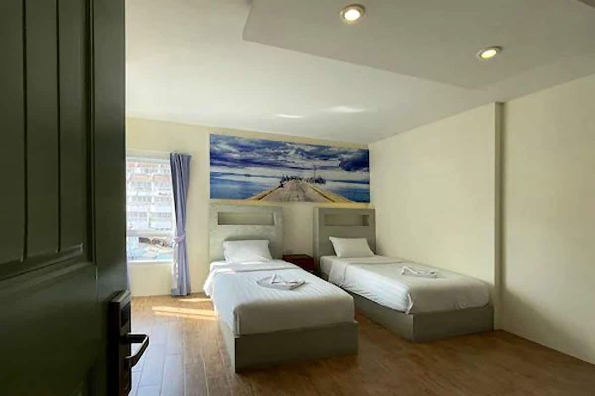 A hotel room with two single beds, a large painting of a coastal scene, and a window with curtains.