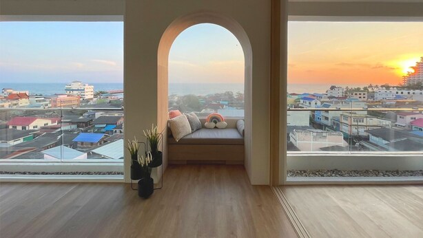 Una habitación con un amplio ventanal arqueado, una cama con almohadas y vistas a la ciudad y al atardecer.