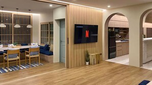 Una sala de estar moderna con comedor, televisor montado en una pared de paneles de madera y cocina integrada con horno empotrado.