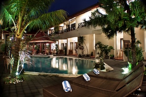 A hotel with a swimming pool, lounge chairs, and a covered area with a thatched roof. - Hotel The Flora Kuta Bali (Kuta)