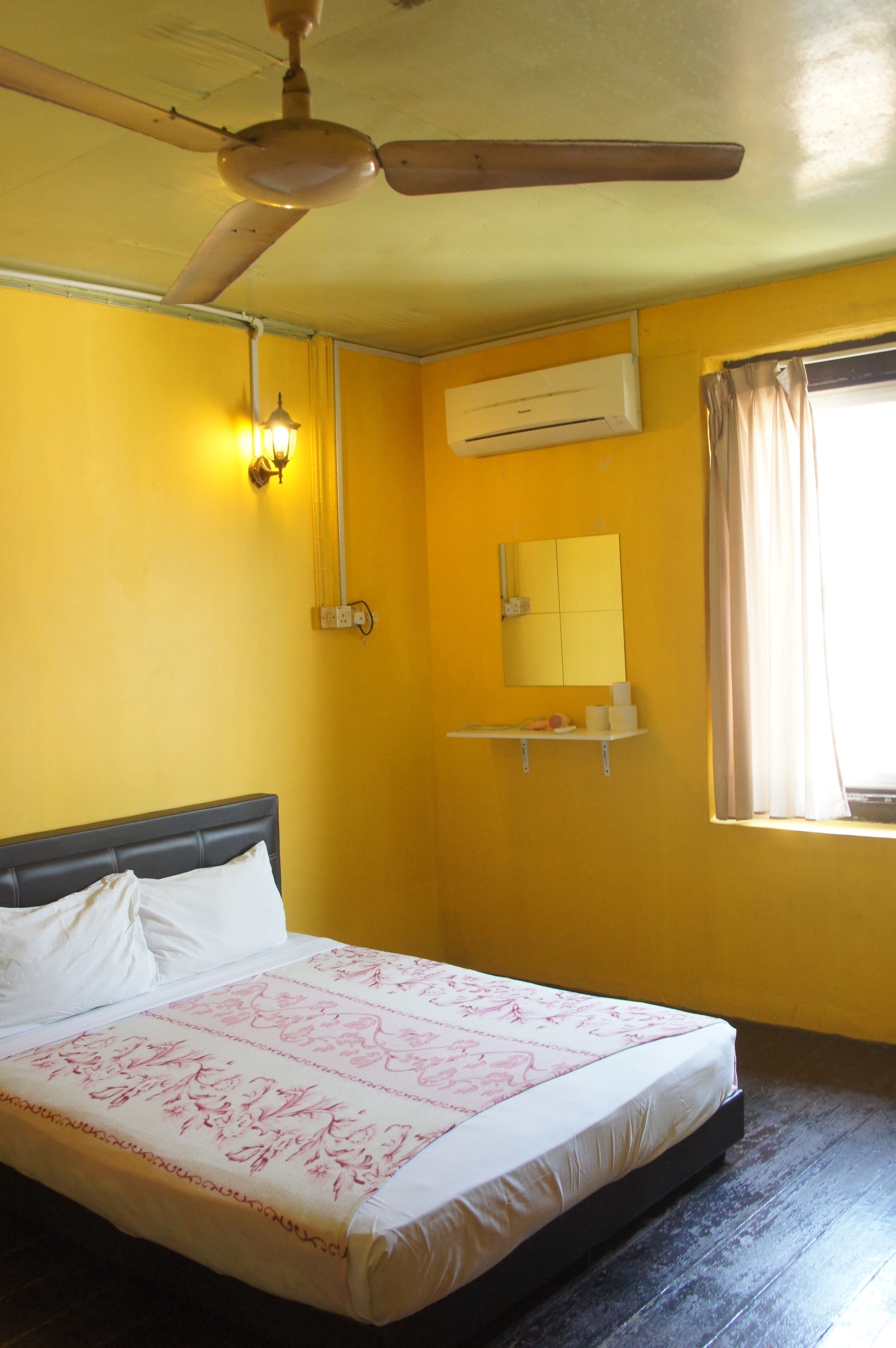 Una habitación con cama, ventilador de techo, aire acondicionado, espejo y ventana con cortinas.