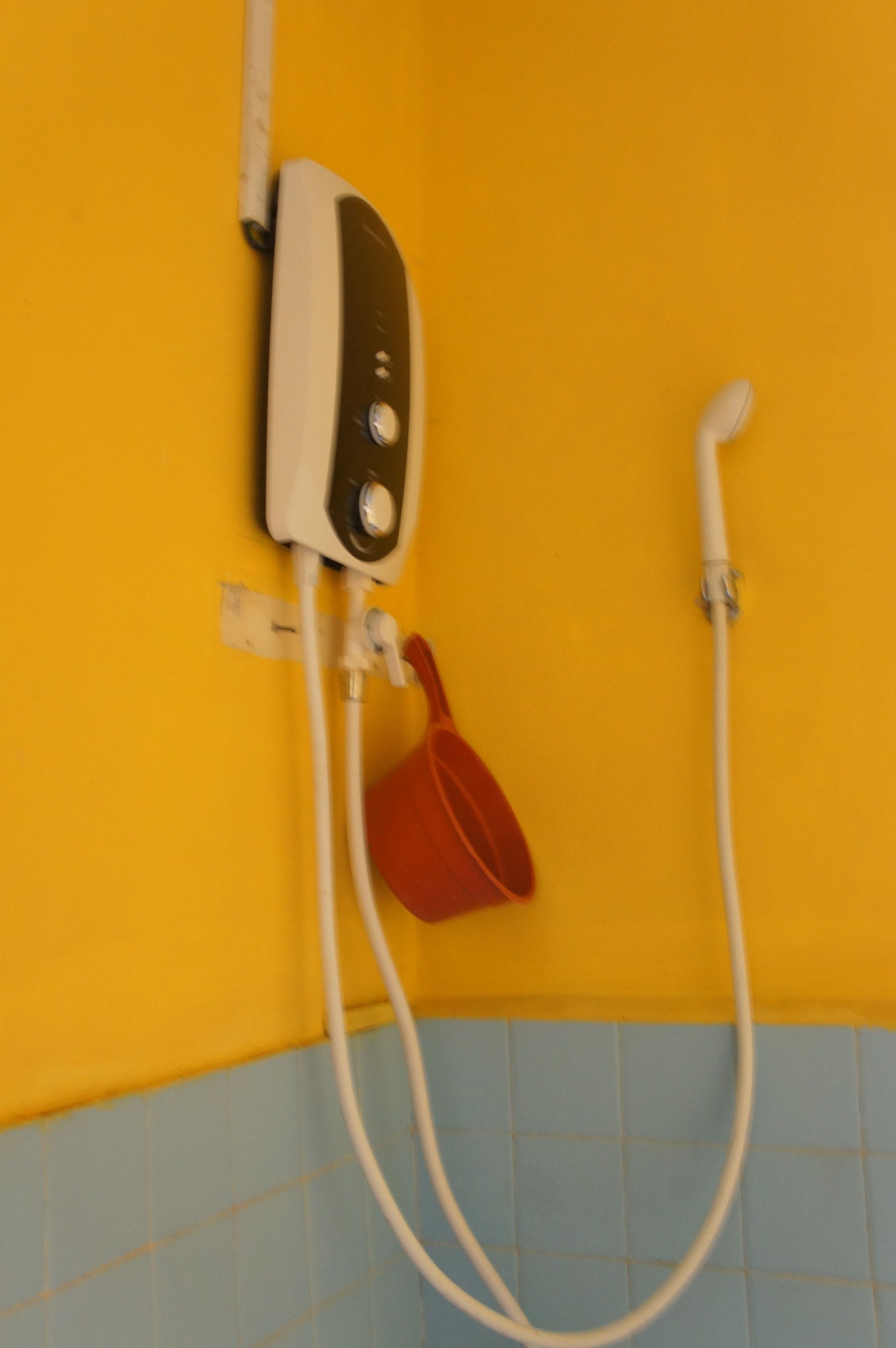Un baño con una pared amarilla, una cabina de ducha blanca y un cubo rojo.