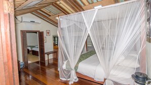 A room with a wooden floor, a bed with a mosquito net, a wooden bench, a table, and a wall-mounted heater. - Noordin Street House (George Town)