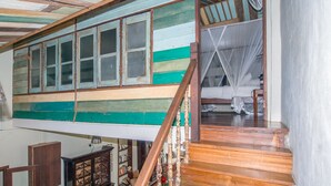 A room with a high ceiling, wooden beams, a staircase with a wooden railing, and a bed with a mosquito net. - Noordin Street House (George Town)