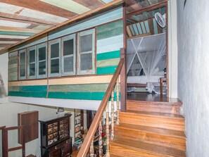 A room with a high ceiling, wooden beams, a staircase with a wooden railing, and a bed with a mosquito net. - Noordin Street House (George Town)