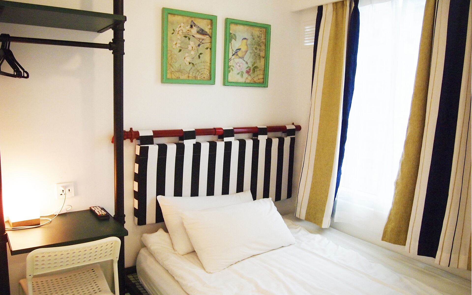 Ein Schlafzimmer mit gestreifter Kopfteil, einem Bett mit weißer Bettwäsche, einem Schreibtisch mit Stuhl und zwei gerahmten Bildern an der Wand.
