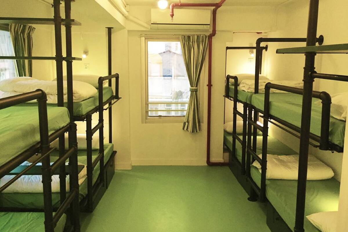 A dormitory room with bunk beds, a window with curtains, and a radiator.