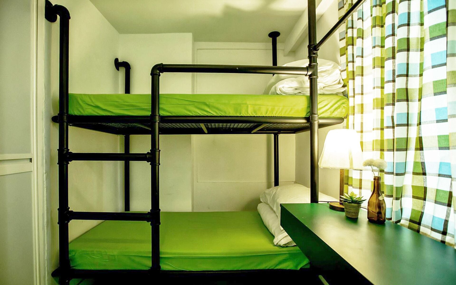 A bunk bed room with green bedding and a table with a lamp and a plant.