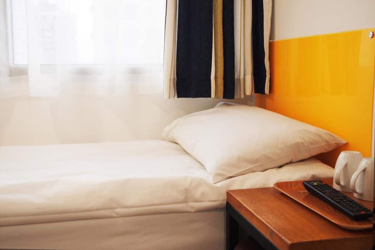 A hotel room with a bed, a wooden nightstand, a remote control, and a white telephone.