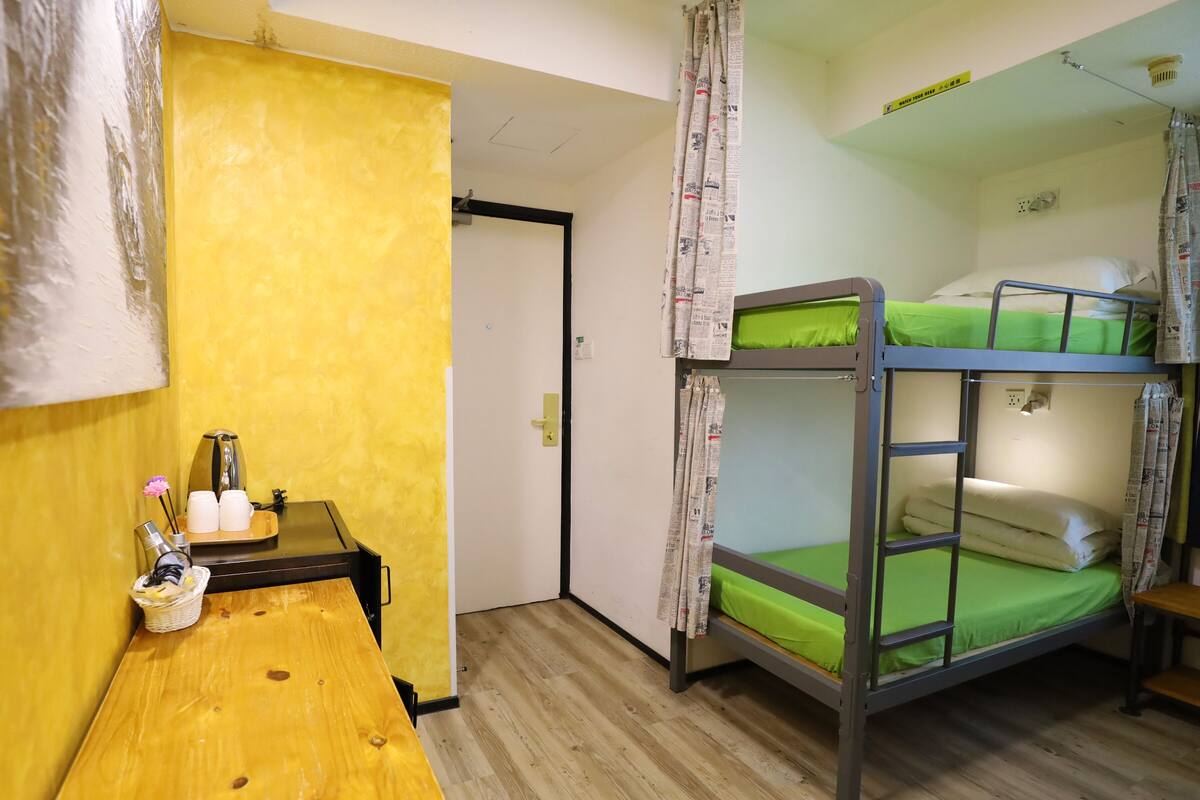 A bunk bed room with a wooden desk, a kettle, and a basket with flowers.