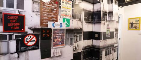 Un mur orné de divers panneaux et affiches, notamment un panneau indiquant « Départ avant 11 heures », un panneau « Interdiction de fumer » et un écran numérique affichant « 2 12 ».