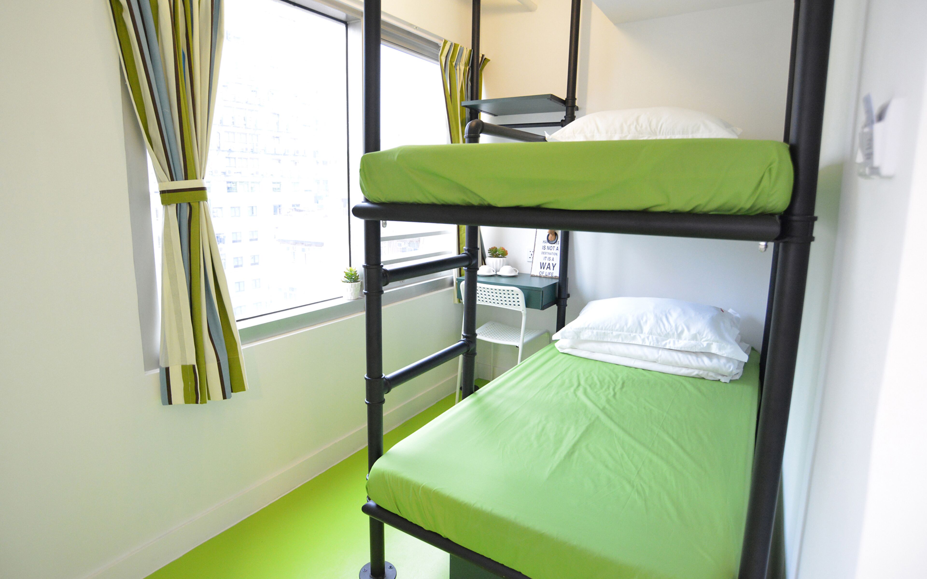 A bunk bed room with a green mattress, a small table with a plant, and a window with curtains.