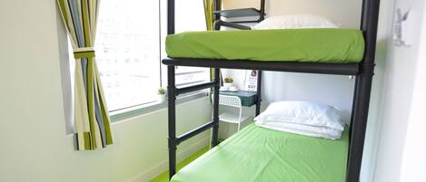 A bunk bed room with a green mattress, a small table with a plant, and a window with curtains.