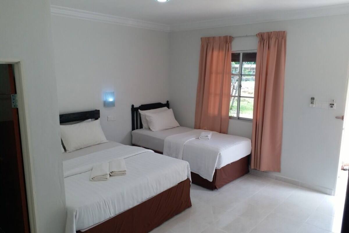 Une chambre d’hôtel avec deux lits, une fenêtre avec des rideaux et un luminaire fixé au mur.