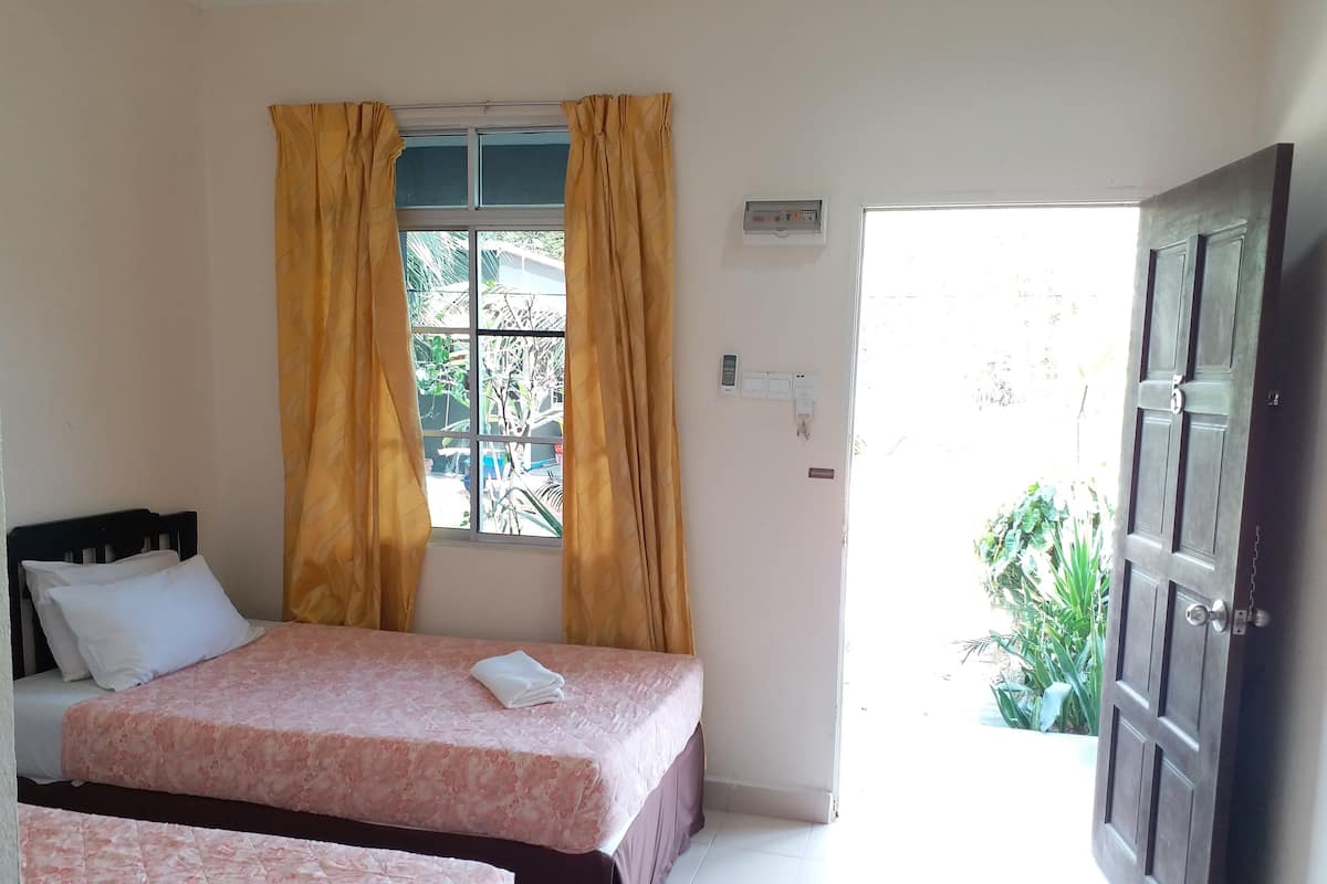 Une chambre avec deux lits, une fenêtre avec des rideaux, une porte et une vue sur l’extérieur.