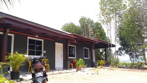A house with a motorcycle parked in front, a porch with chairs, and a view of trees and hills in the background. - Idaman Guesthouse (Langkawi)