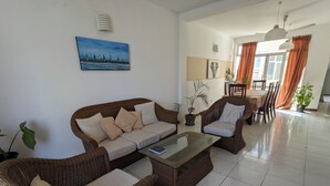 A living room with a sofa, armchairs, a coffee table, and a dining area with a table and chairs. There is a painting on the wall and a potted plant. - Palmyrah Residencies (Colombo)