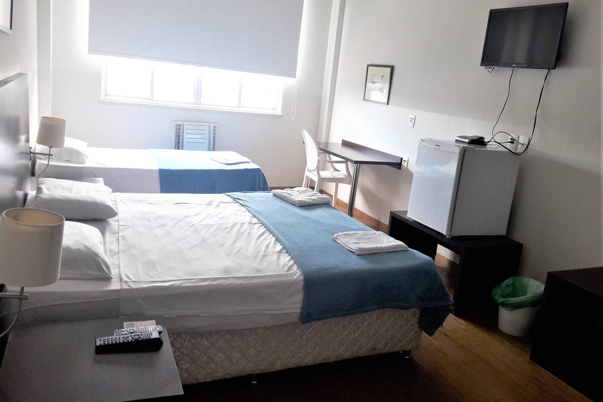 Une chambre d’hôtel avec deux lits, un bureau, une chaise, une télévision et un petit réfrigérateur.