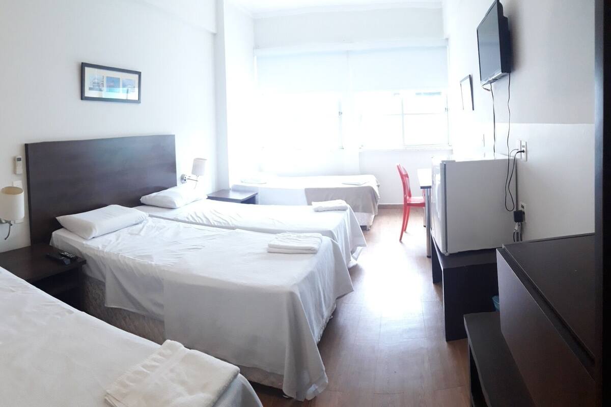 Une chambre d’hôtel avec deux lits simples, un grand miroir, une table de chevet avec une lampe, une télévision et un petit bureau.