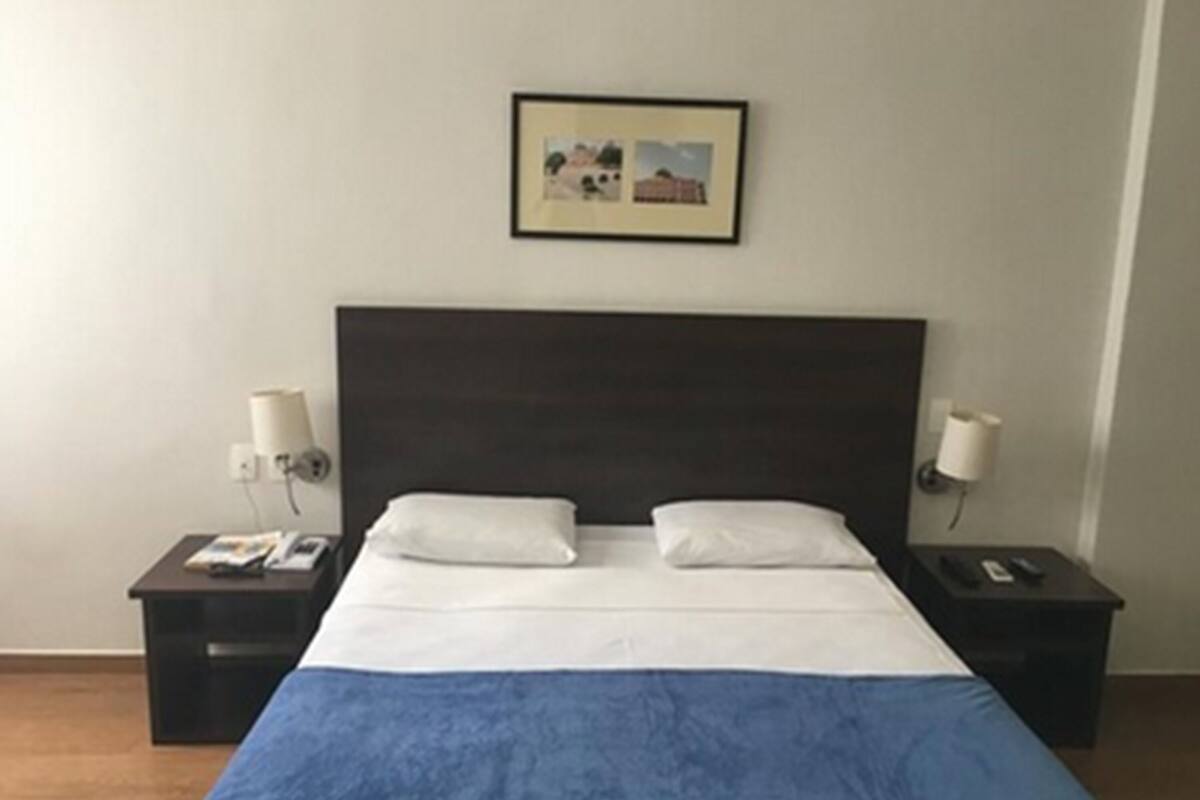Une chambre d’hôtel avec un grand lit, deux tables de chevet, une petite table et un tableau encadré au mur.
