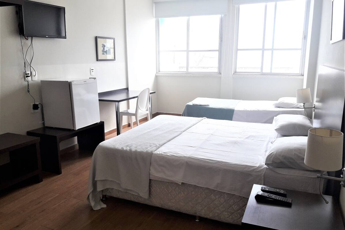 Une chambre d’hôtel dotée d’un grand lit, d’un bureau, d’une chaise, d’un téléviseur fixé au mur et d’une fenêtre laissant entrer la lumière naturelle.