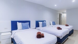 Habitación de hotel con tres camas, cada una con ropa de cama blanca y cabeceros azules. Hay mesitas de noche blancas y un pequeño escritorio con una silla.