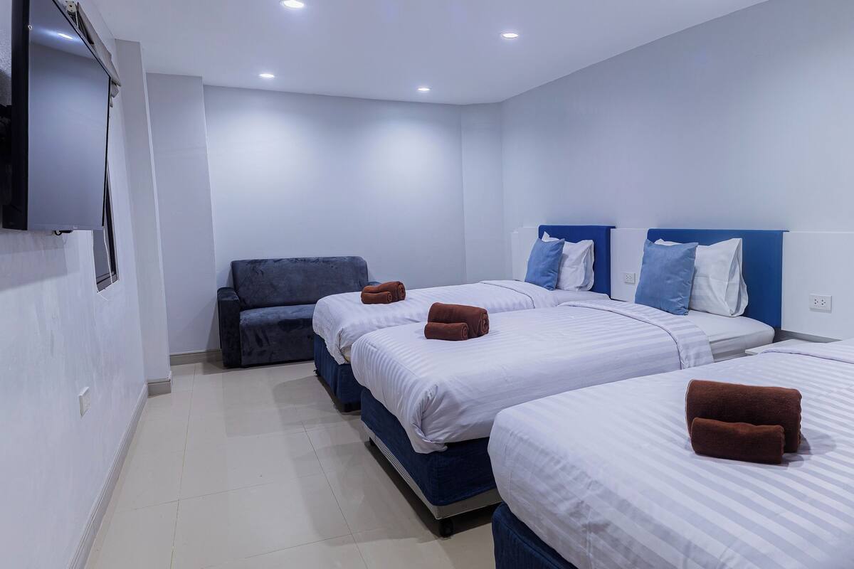 A hotel room with three beds, a sofa, and a flat-screen TV.