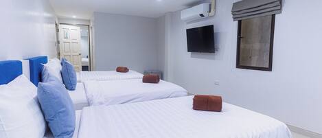 A hotel room with two beds, a TV, an air conditioning unit, and a window with a curtain.