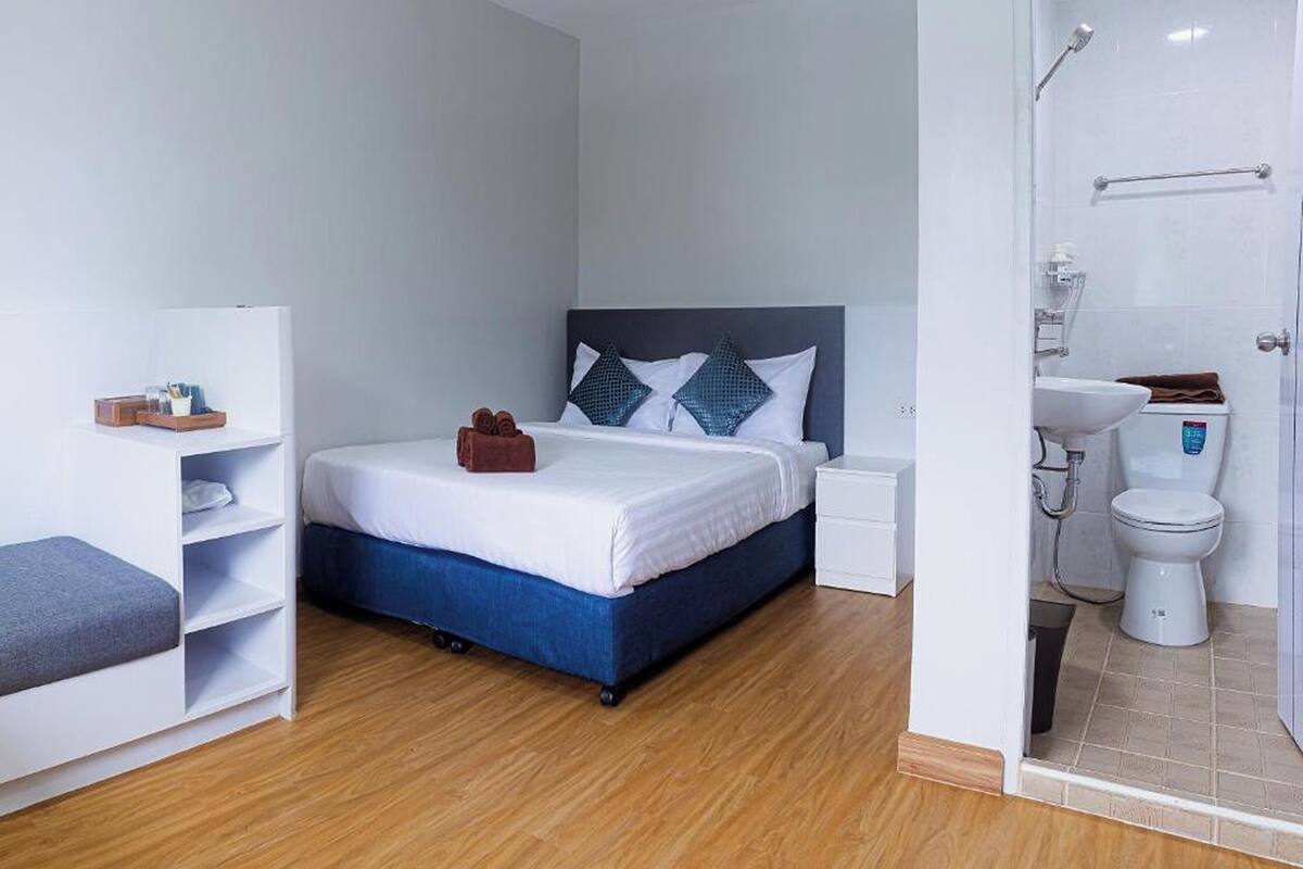 A modern hotel room with a bed, bedside tables, a wardrobe, and a bathroom with a toilet and shower.